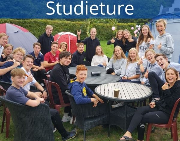 Billedet viser en stor gruppe elever på studietur samlet i afslappede omgivelser med telte og fælles samvær. Motivet signalerer fællesskab, glæde og oplevelser, der styrker relationer uden for klasselokalet.